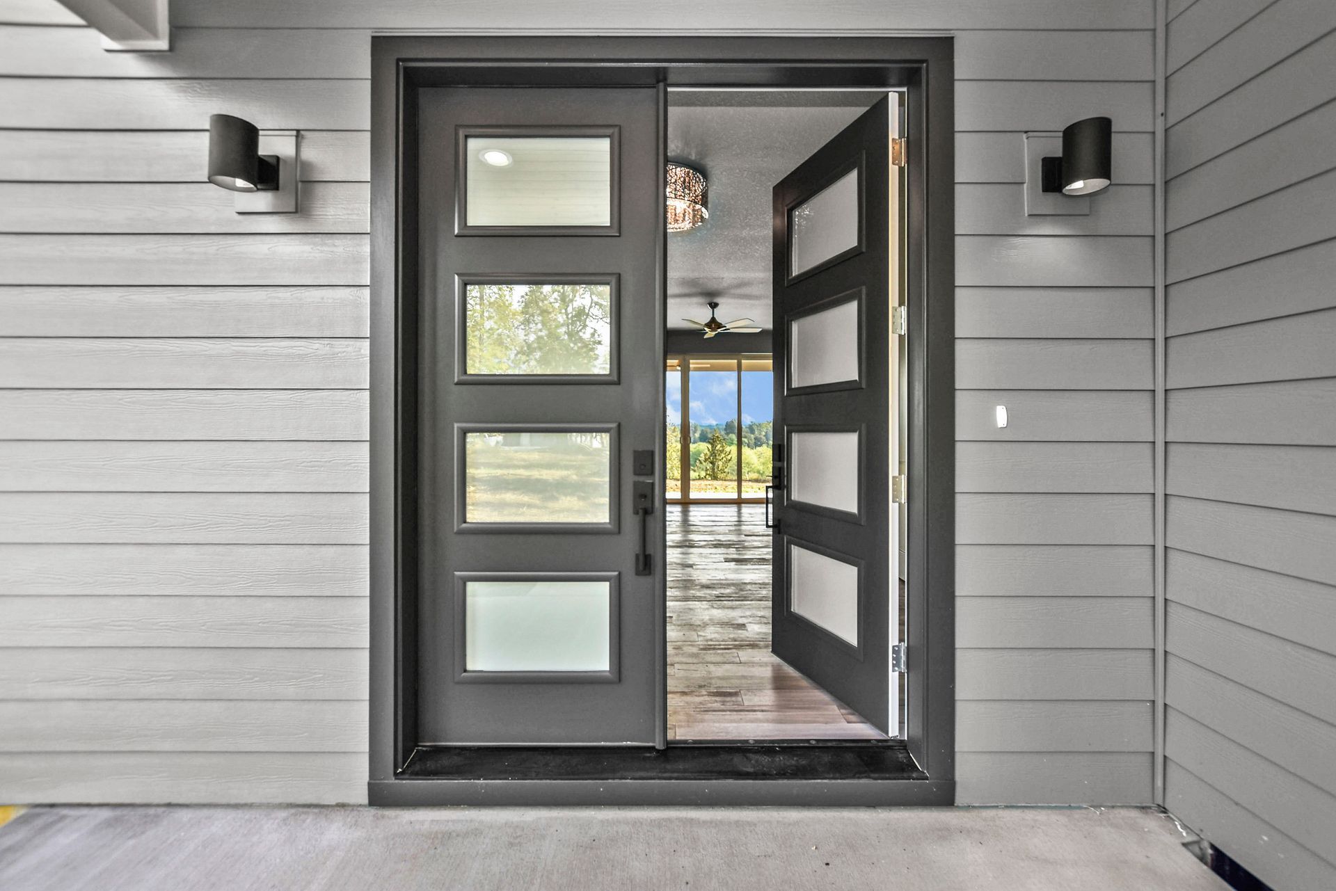 Modern black front door with frosted glass panels, open to a bright interior on a gray exterior wall