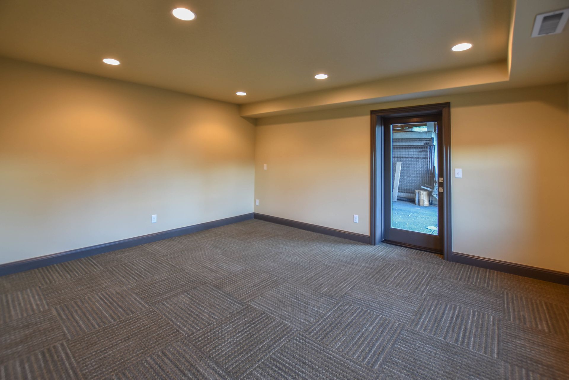 Empty carpeted room with beige walls, recessed lights, and a glass door to the outside.