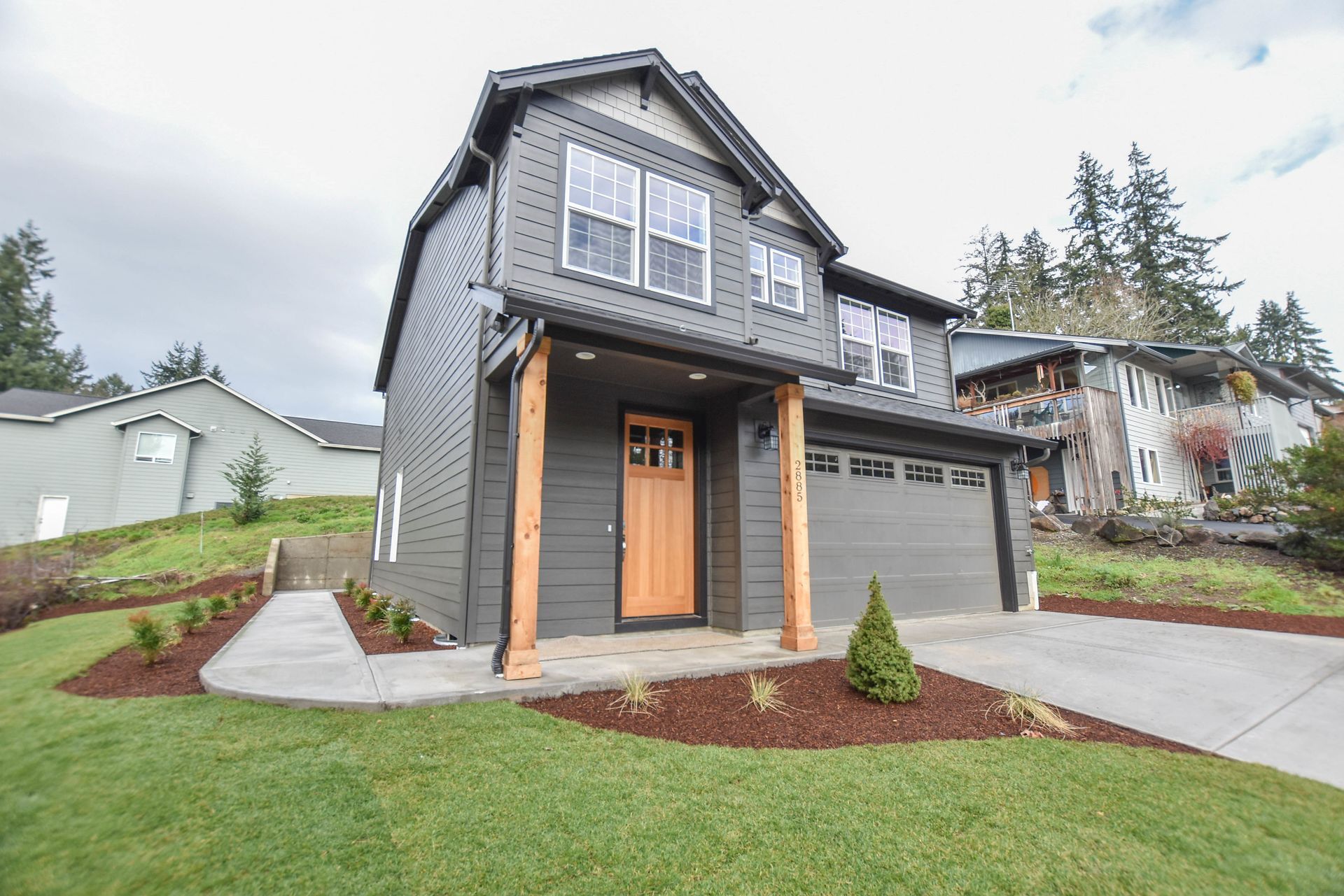 Modern gray two-story house with wood front porch, garage, and landscaped lawn