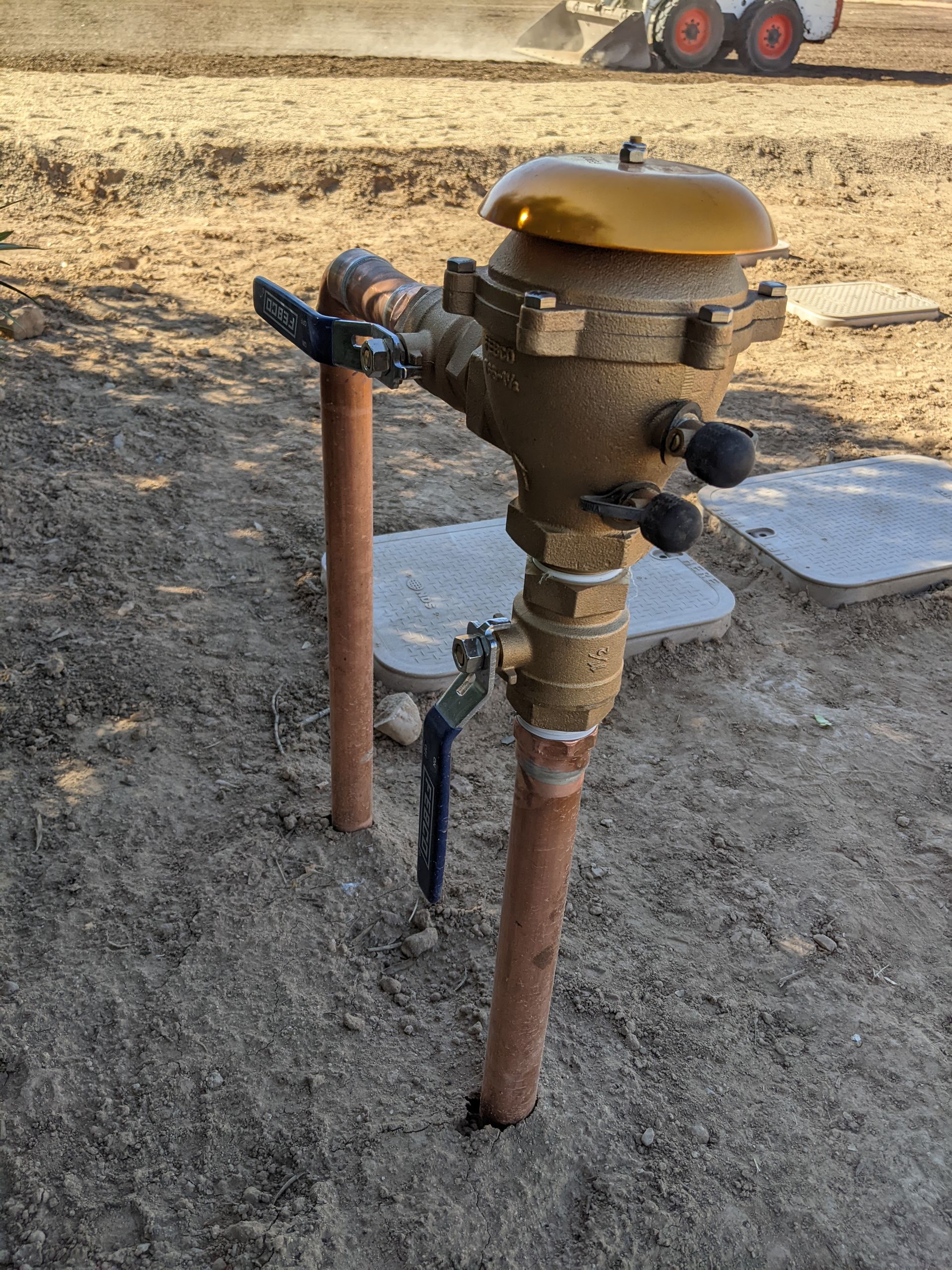 Hands holding a dark gray PVC ball valve with a red handle. Other plumbing parts are in the background.