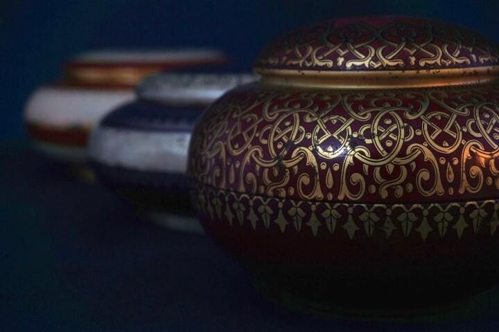Three ornate, round jars in a row; dark red jar in focus with gold filigree design.