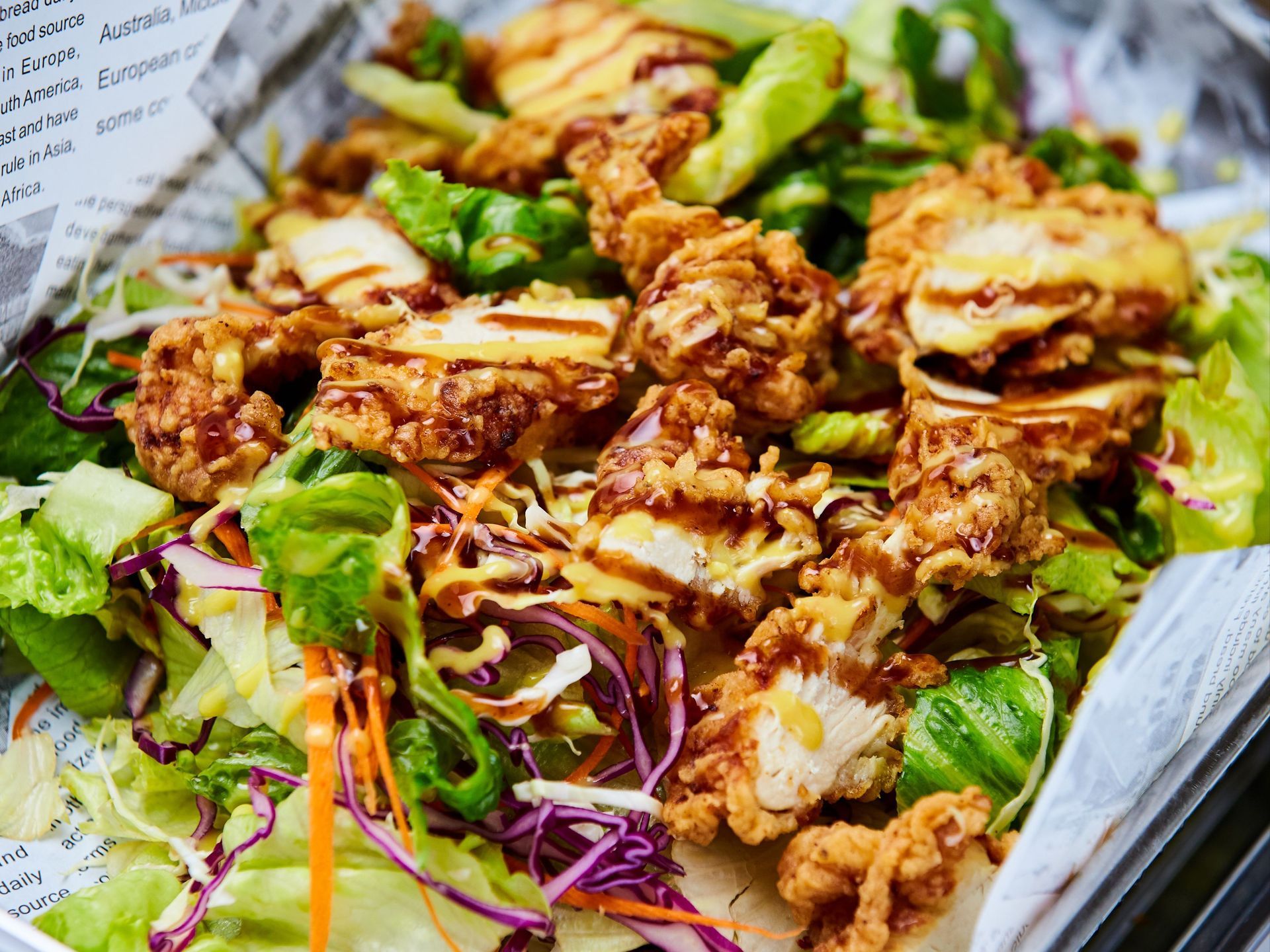 Grilled chicken salad in a silver tray with mixed greens and drizzled dressing.