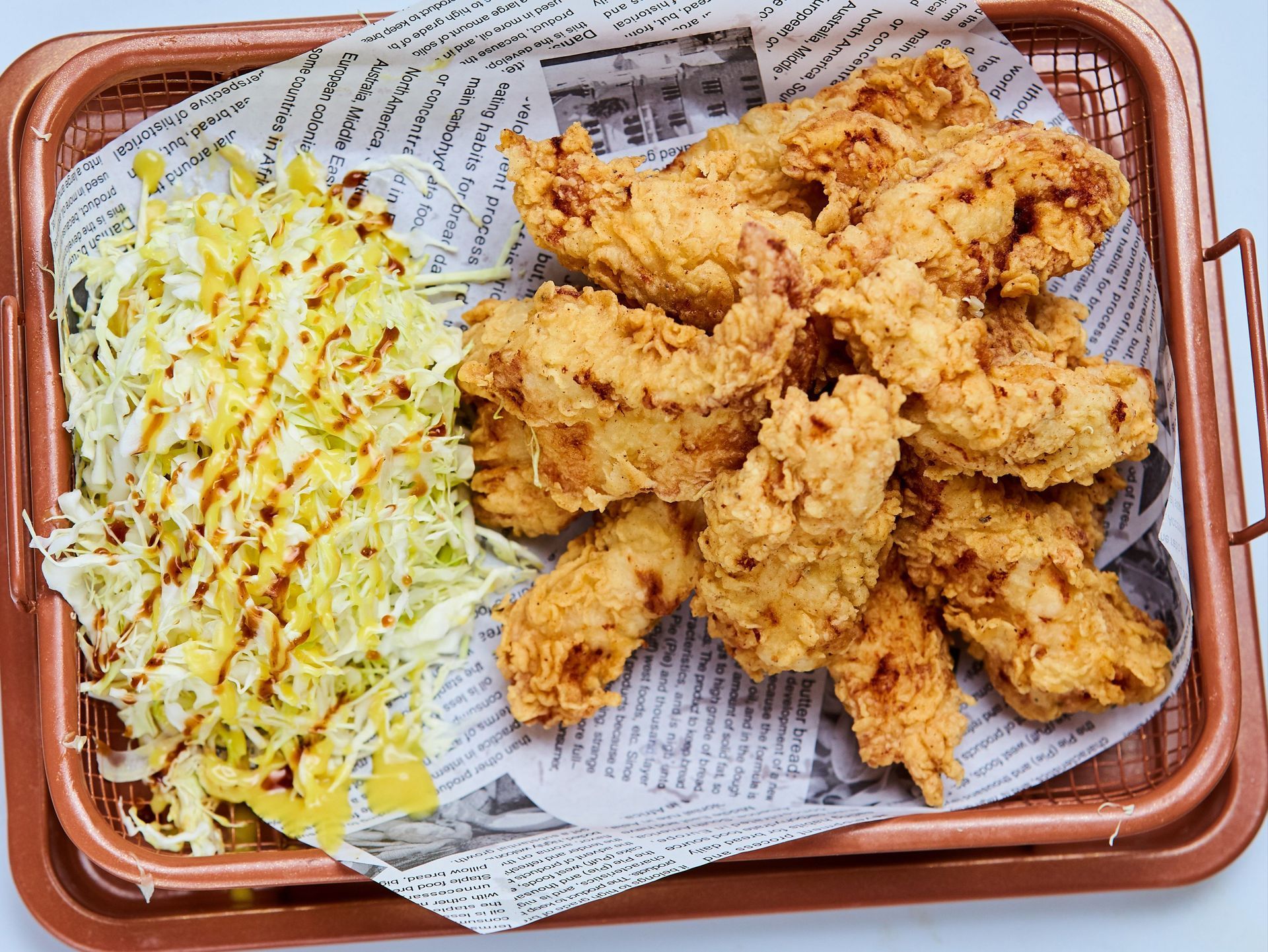 Fried chicken and shredded cabbage on a tray lined with patterned paper.