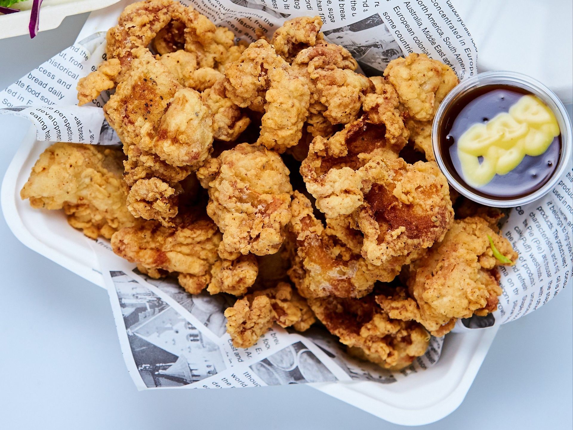 Fried chicken pieces in a container with dipping sauce, and a salad in the background.