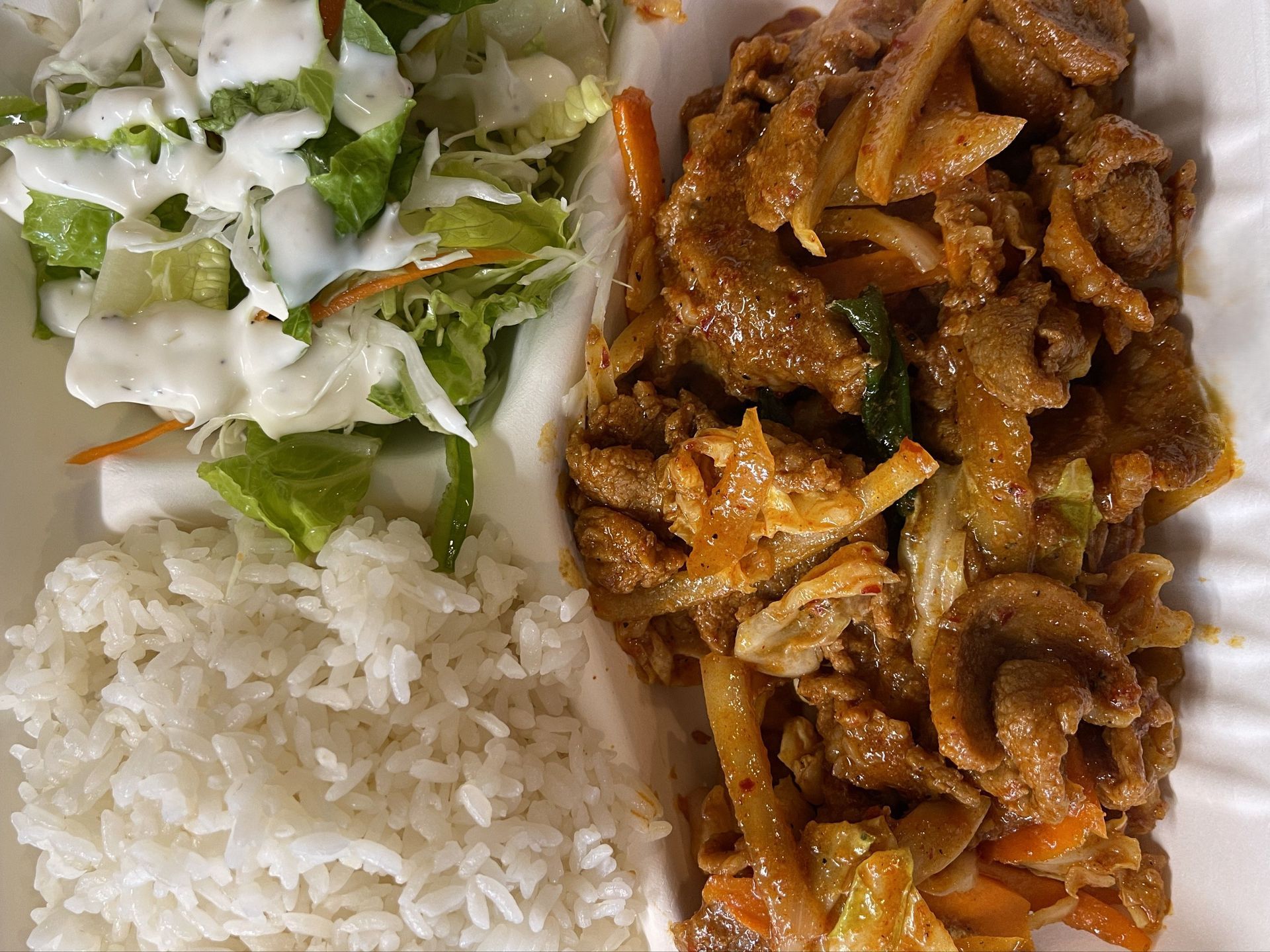 Grilled chicken salad with mixed greens, shredded carrots, and a dark sauce on a silver tray lined with newspaper.