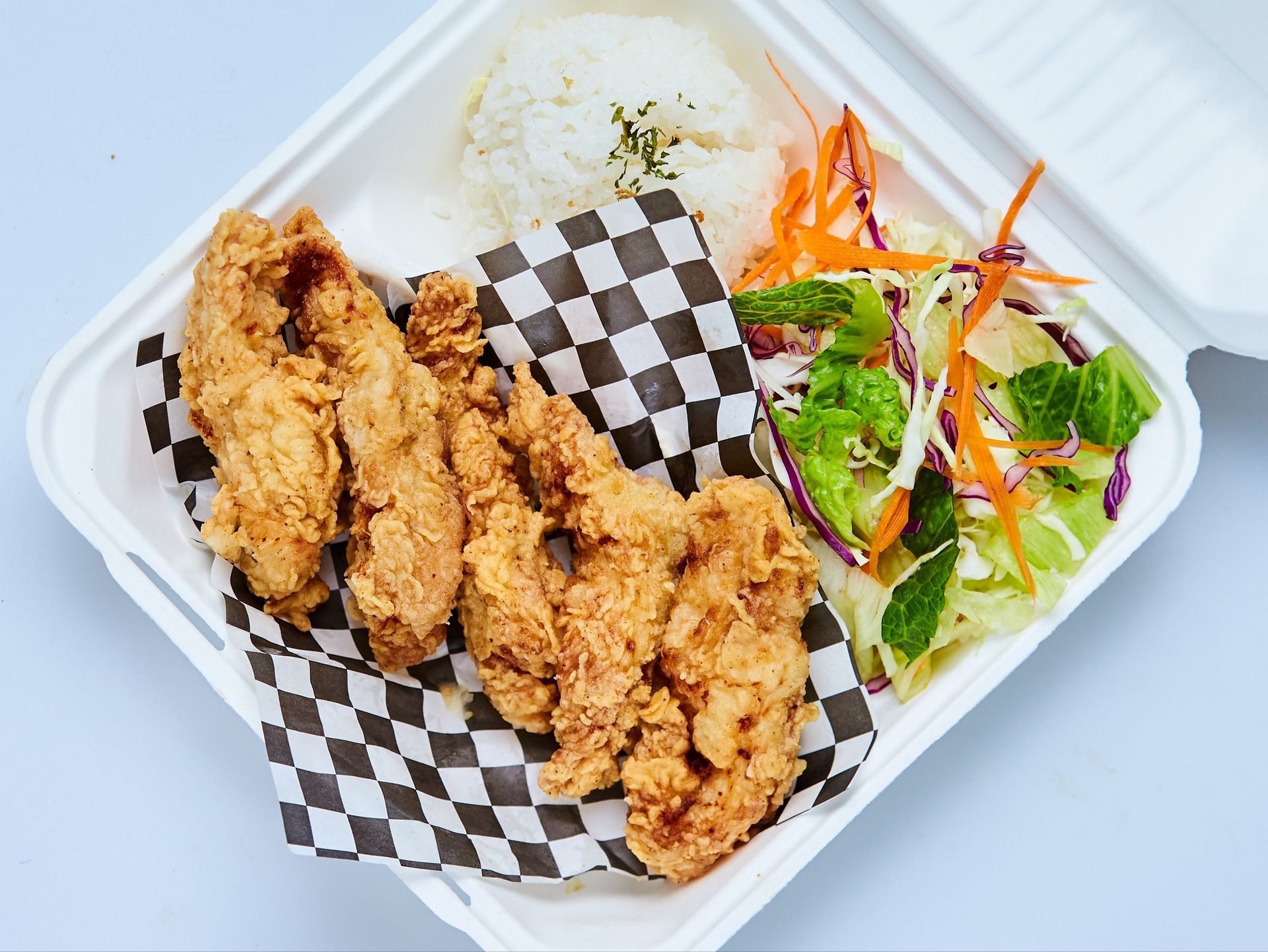 Fried chicken cutlet with rice, salad, and drizzle on a white plate.