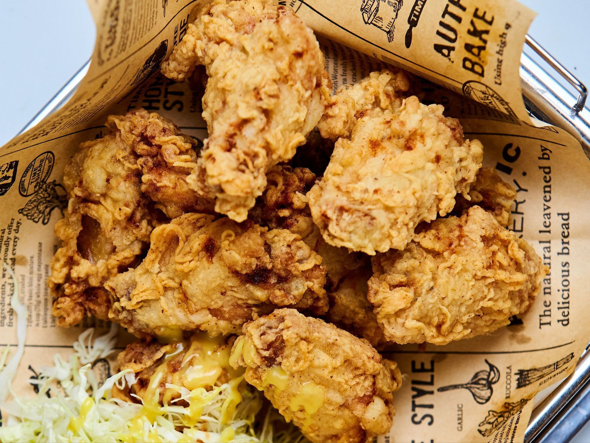 Fried chicken and salad on a white plate, atop newspaper-printed paper. The chicken is golden brown; the salad contains greens and carrots.