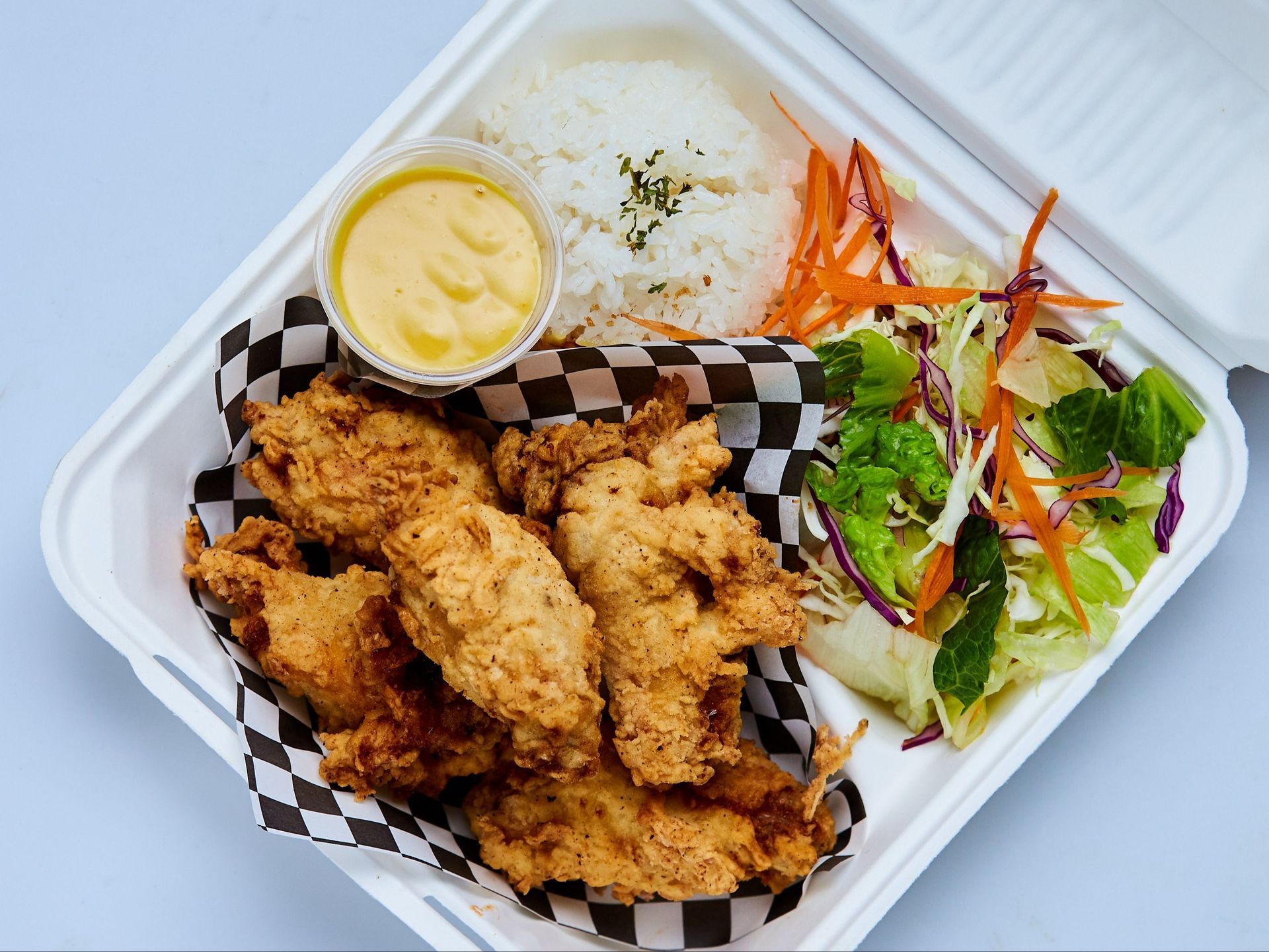Chicken katsu with rice and salad, drizzled with sauce on a white plate.