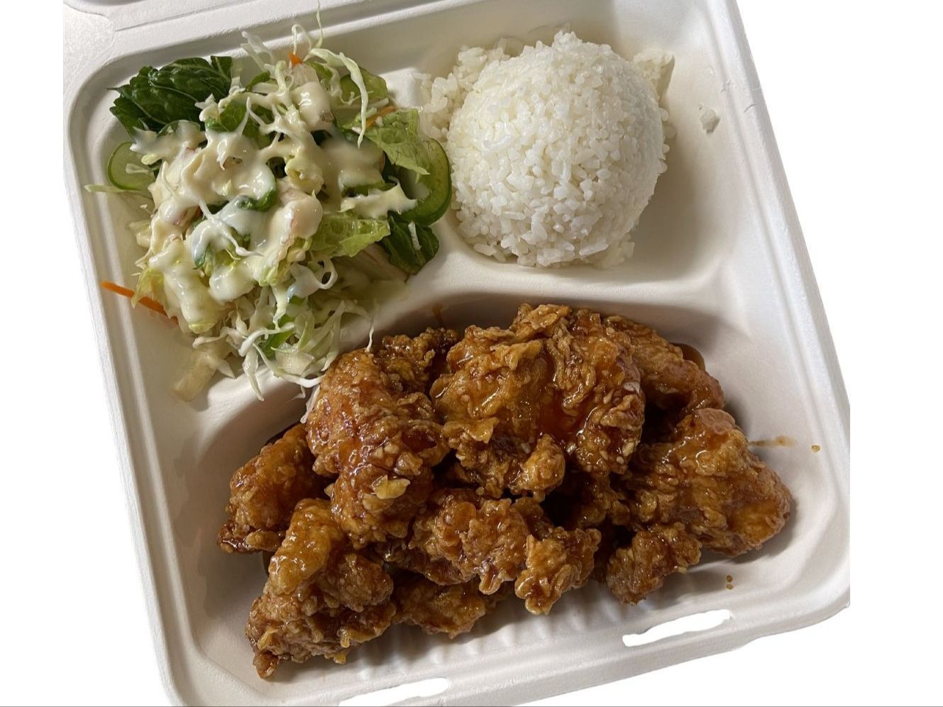 Fried chicken cutlet with rice and salad, drizzled with sauce, on a white plate.