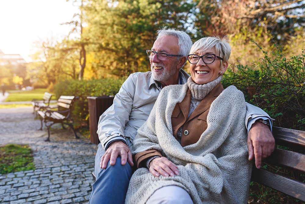 An elderly couple is sitting on a park bench.