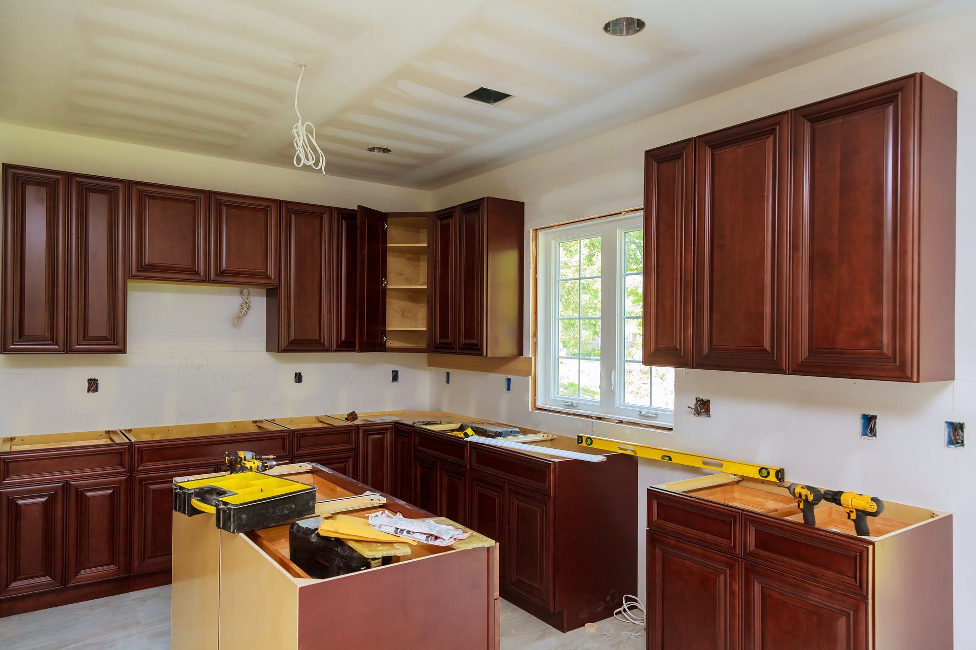 Partially renovated kitchen with dark wood cabinets, countertop boxes, and a window above the sink