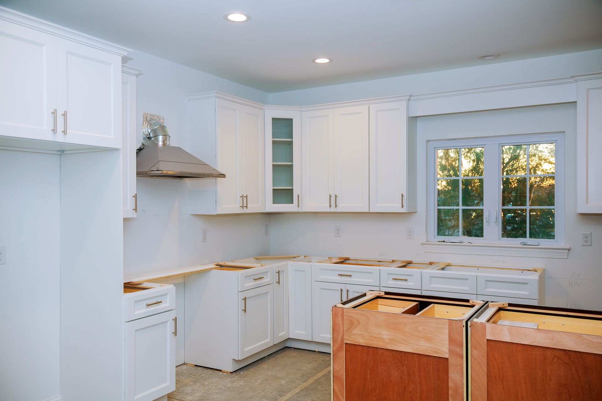 Bright white kitchen with cabinets, window, and unfinished island in the foreground