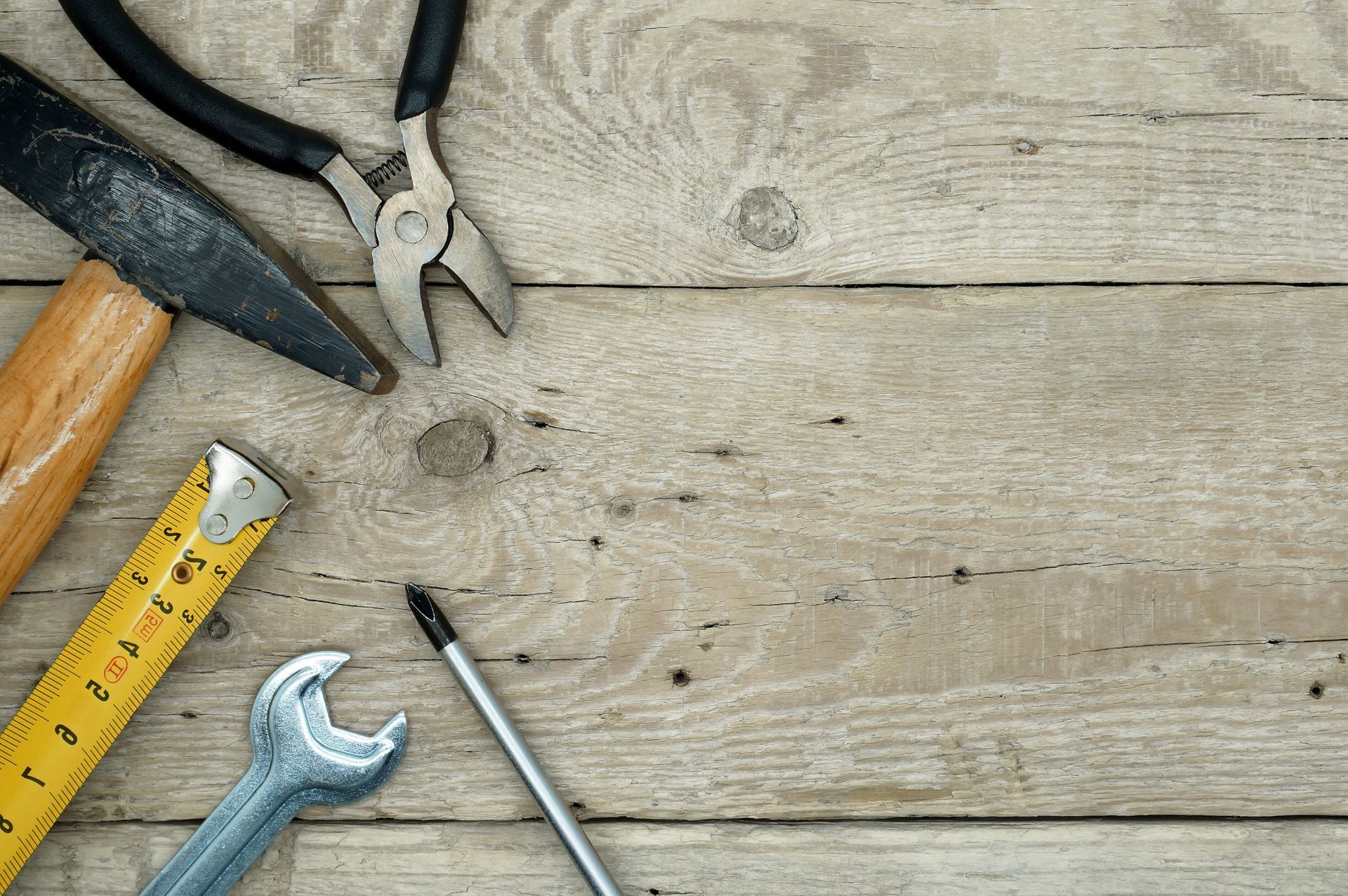 A hammer , pliers , tape measure , wrench and screw on a wooden table.