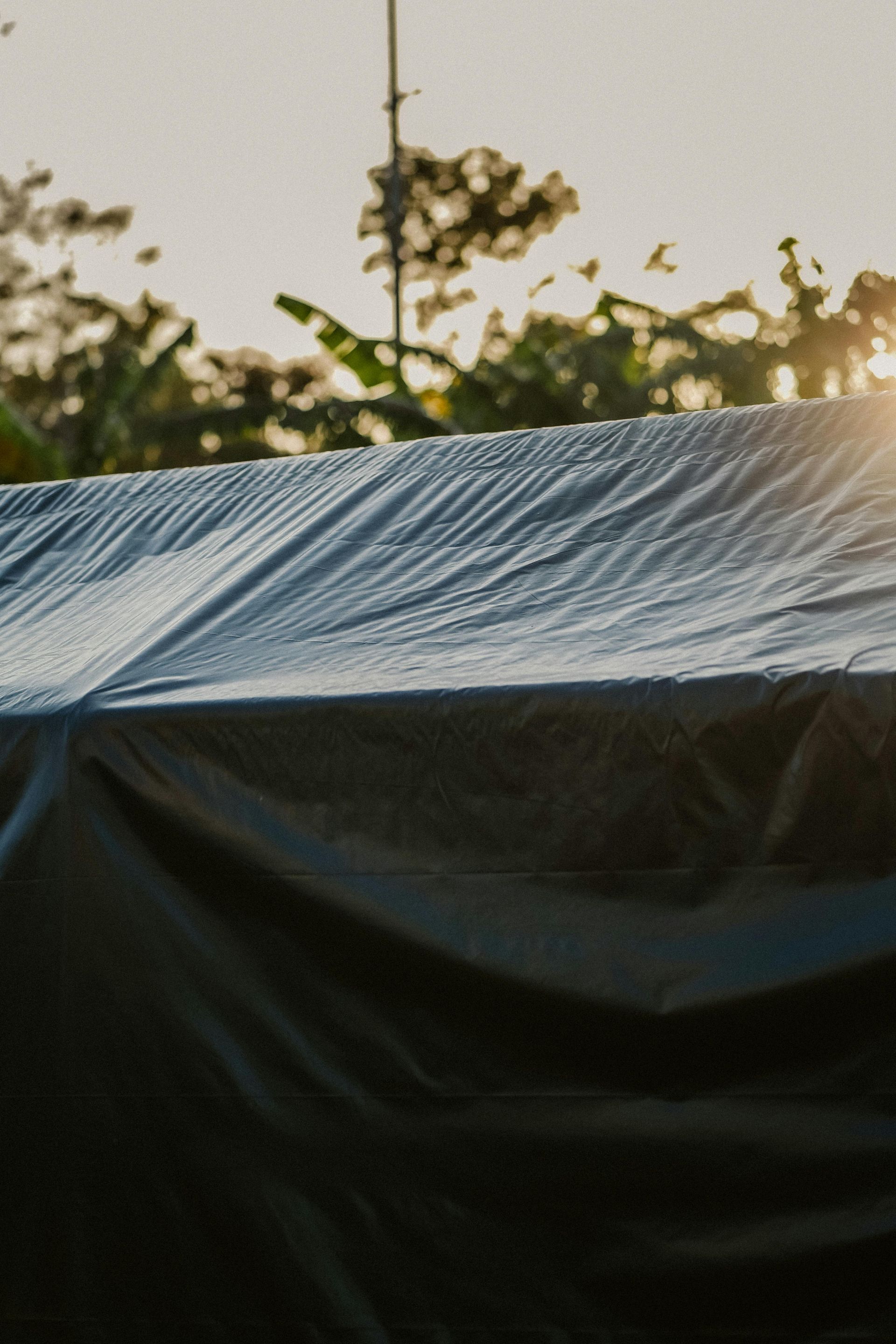 Attic insulation with exposed wooden beams and a small window. Beige spray foam covers the interior.