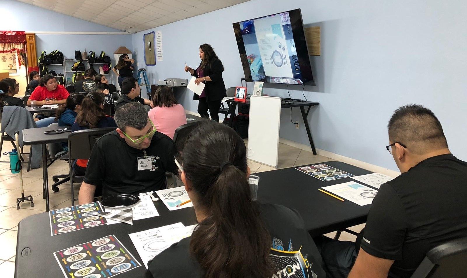 A woman is giving a presentation to a group of people sitting at tables.