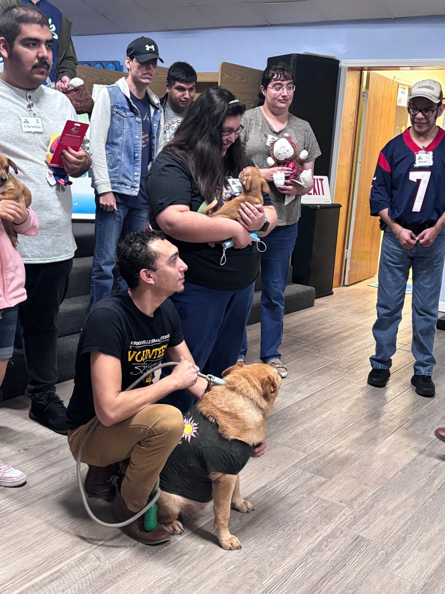 A group of people are standing around a dog in a room.
