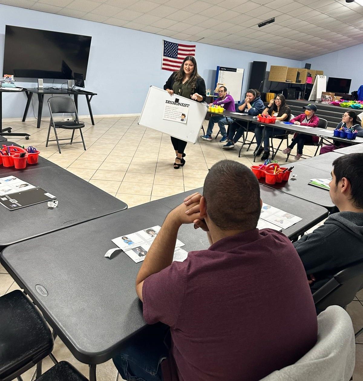 A woman is giving a presentation to a group of people sitting at tables.