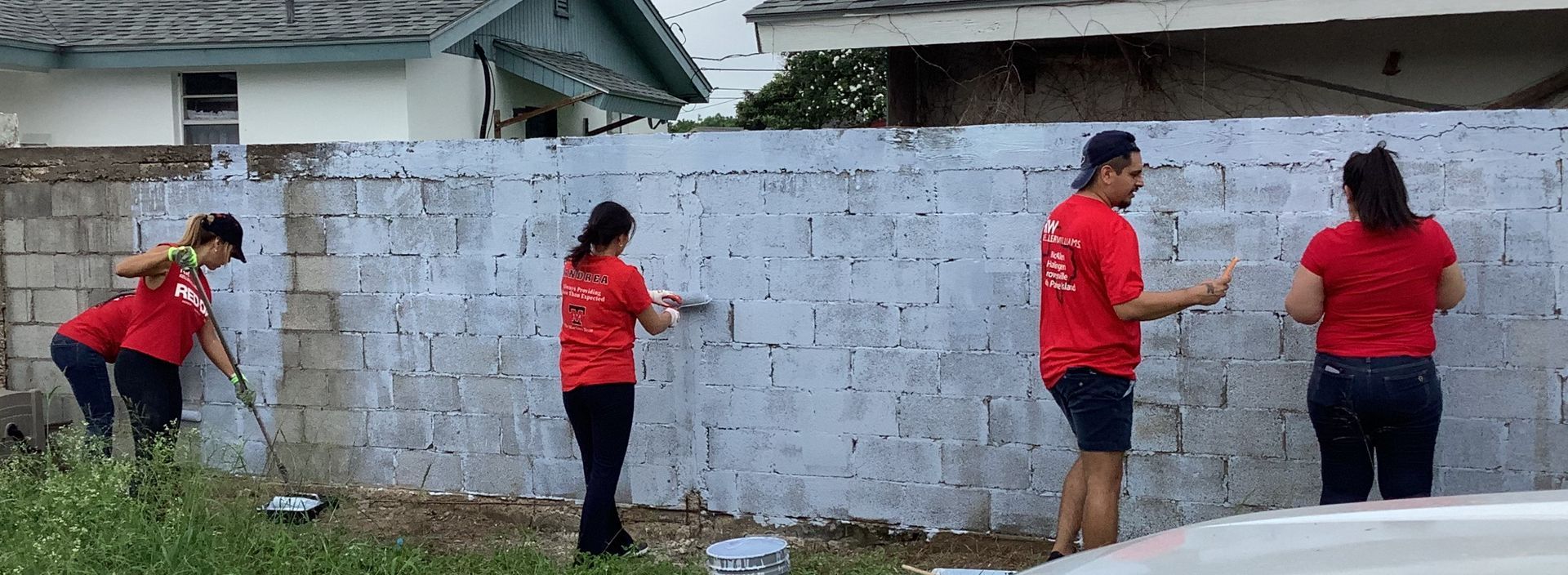 A group of people are painting a white brick wall.