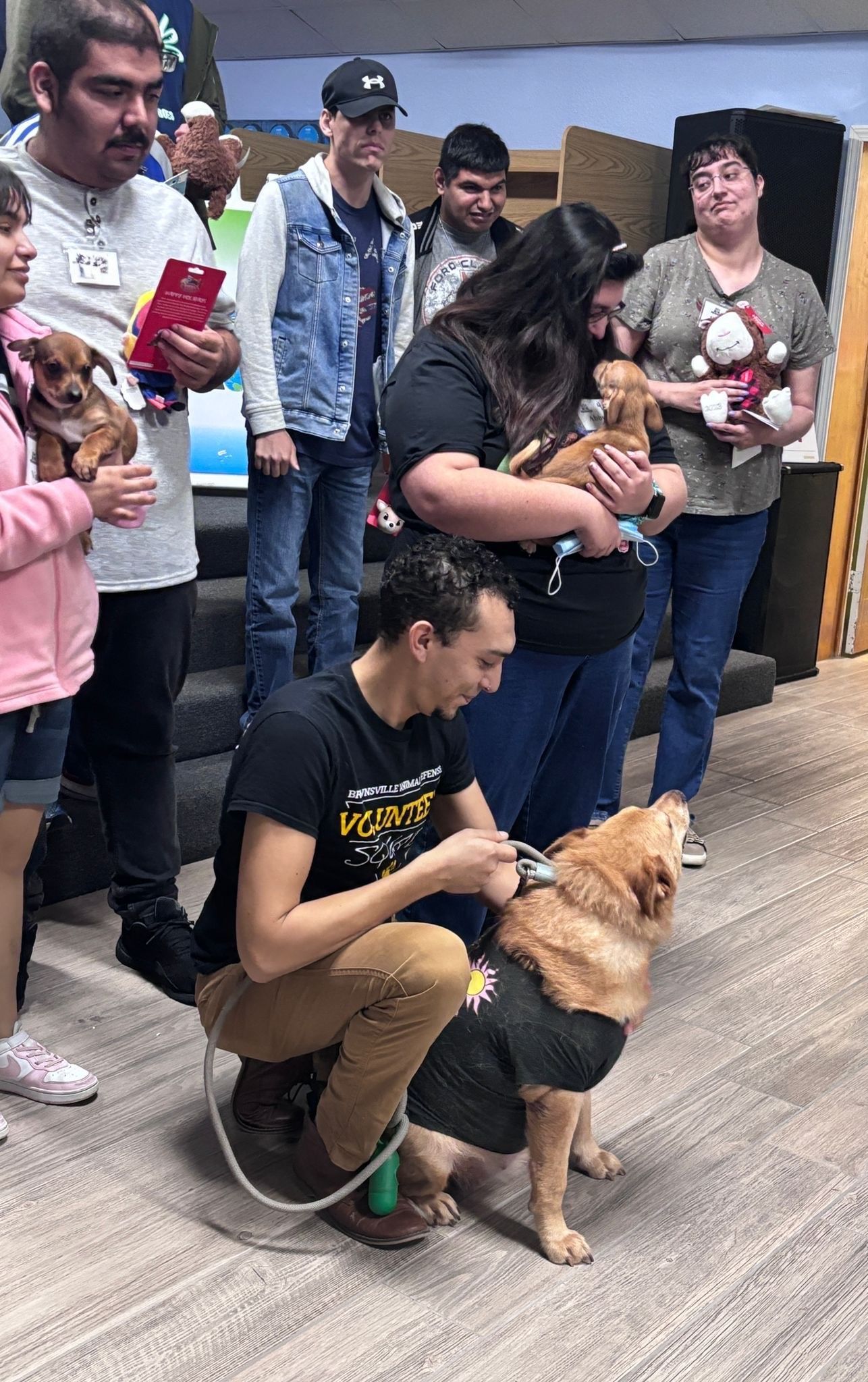 A group of people are standing around a dog in a room.