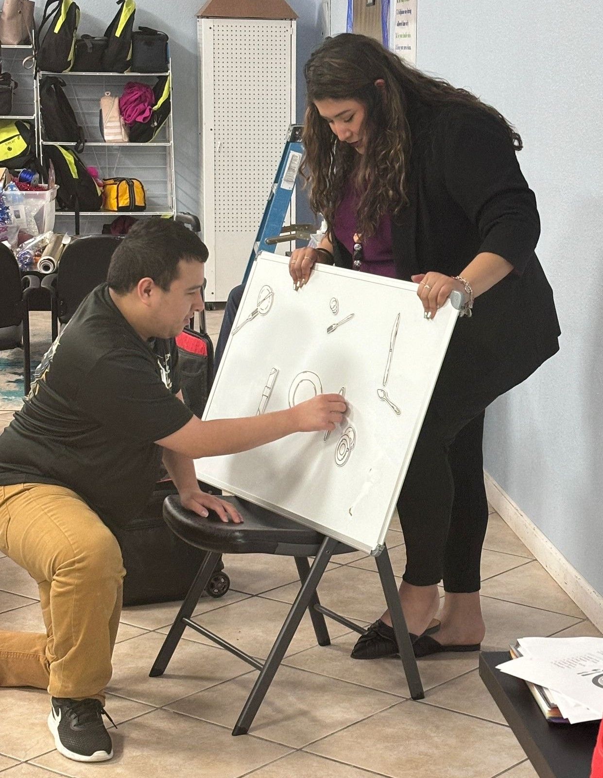 A man and a woman are drawing on a white board