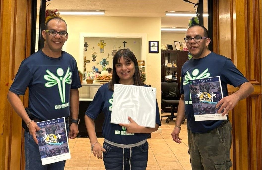 Three people in blue shirts are standing in a doorway holding papers.