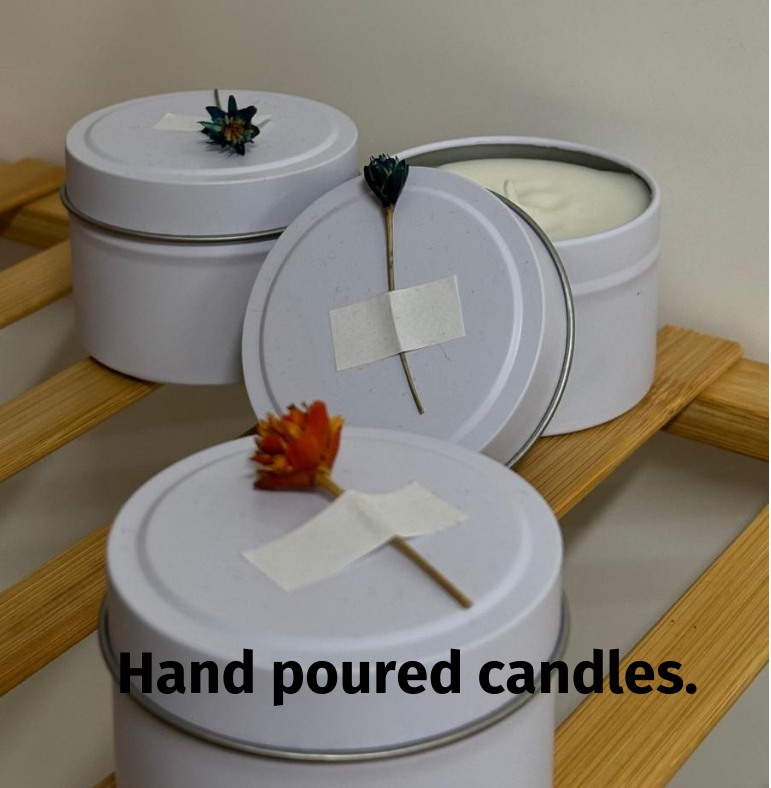 Hand-poured candles in white tins, adorned with dried flowers and tape, displayed on a wooden rack.