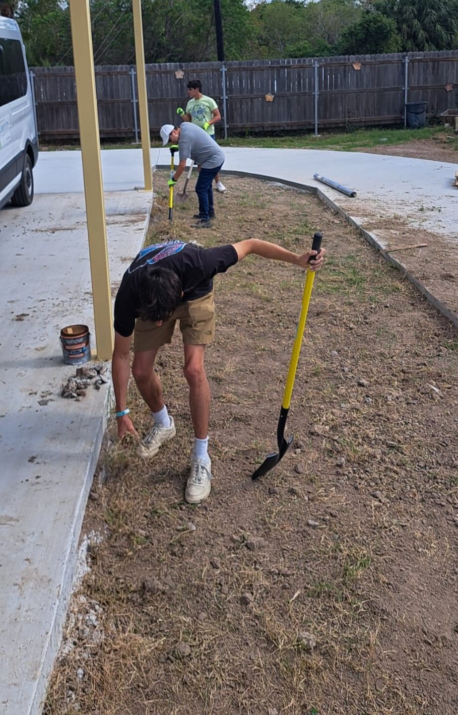 A man is kneeling down in the dirt holding a shovel.