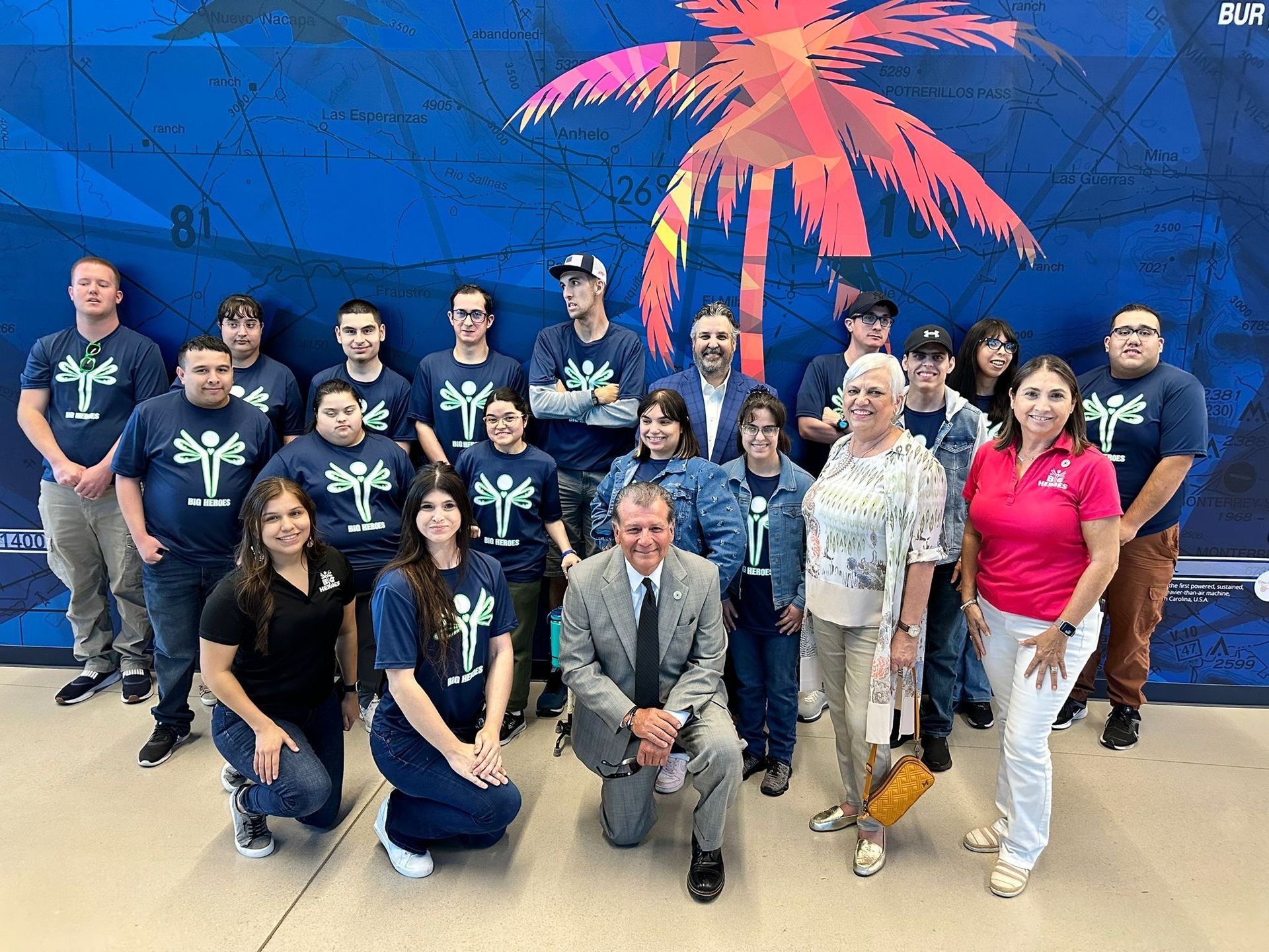 A group of people are posing for a picture in front of a mural of palm trees.