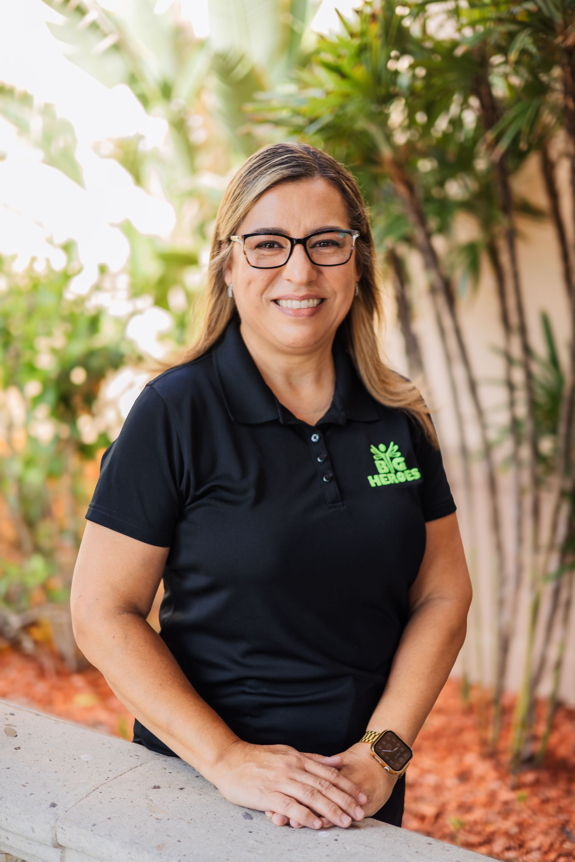 A woman wearing glasses and a black shirt is standing next to a blue bench.