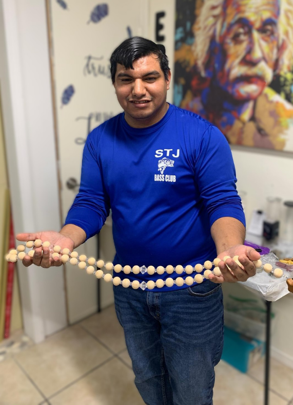 Man in blue shirt, smiling, holding beaded garland. Standing in front of a door and painting.