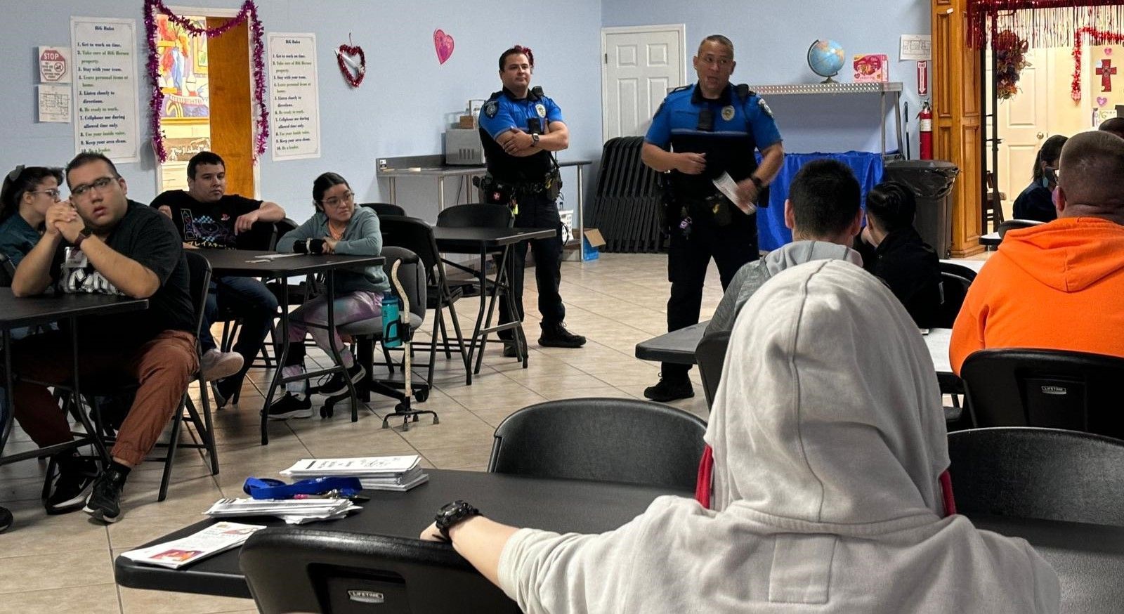 Two police officers are standing in front of a group of people sitting at tables.