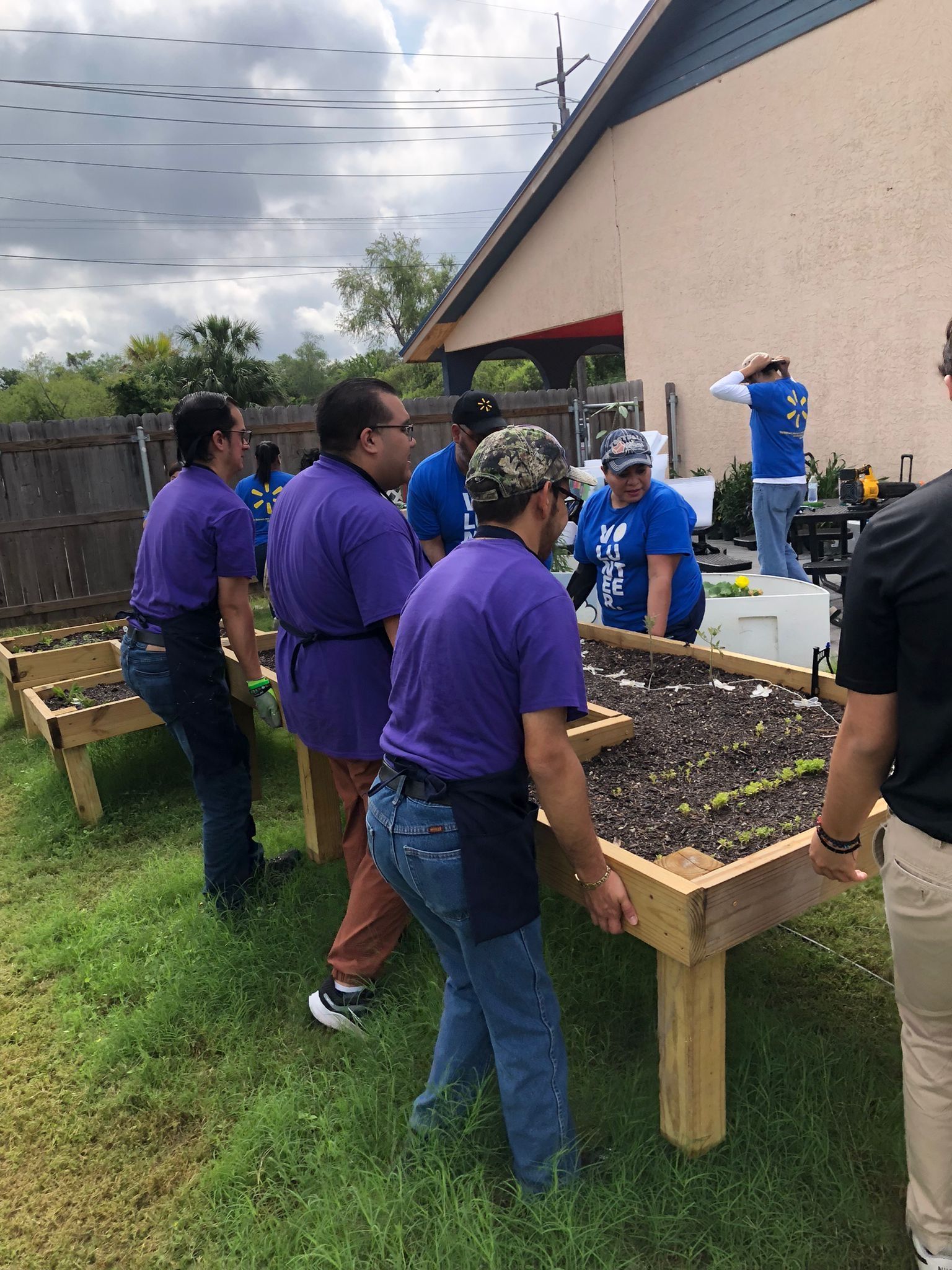 A group of people are standing around a wooden table in a garden.