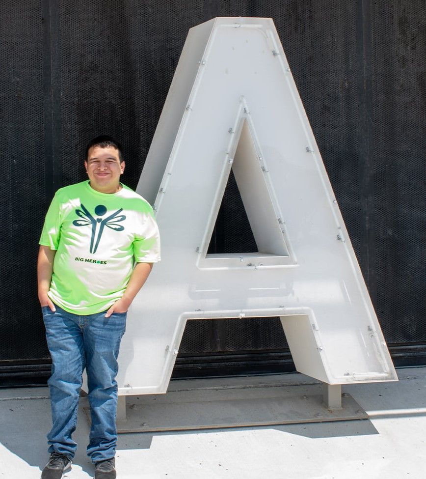 A man in a green shirt stands in front of a large letter a