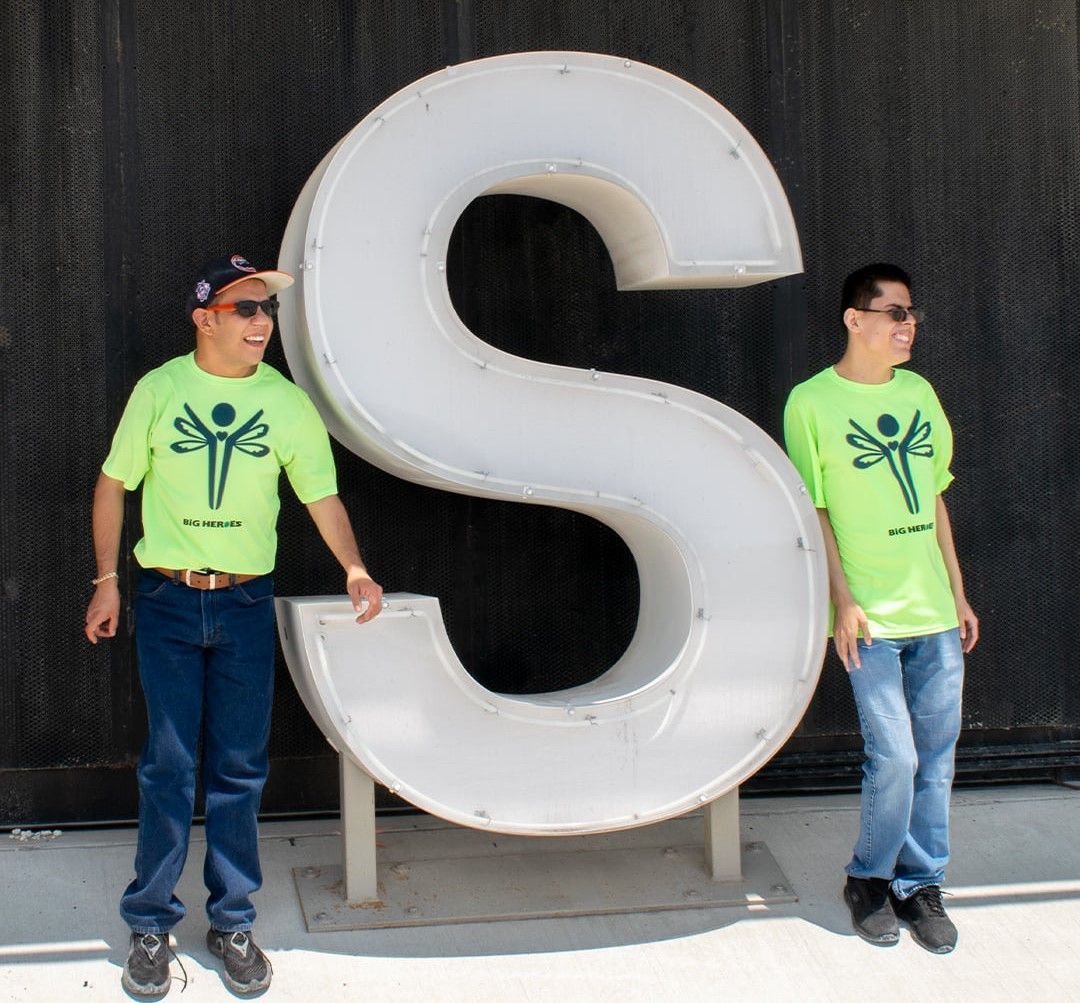 Two men standing next to a large letter s