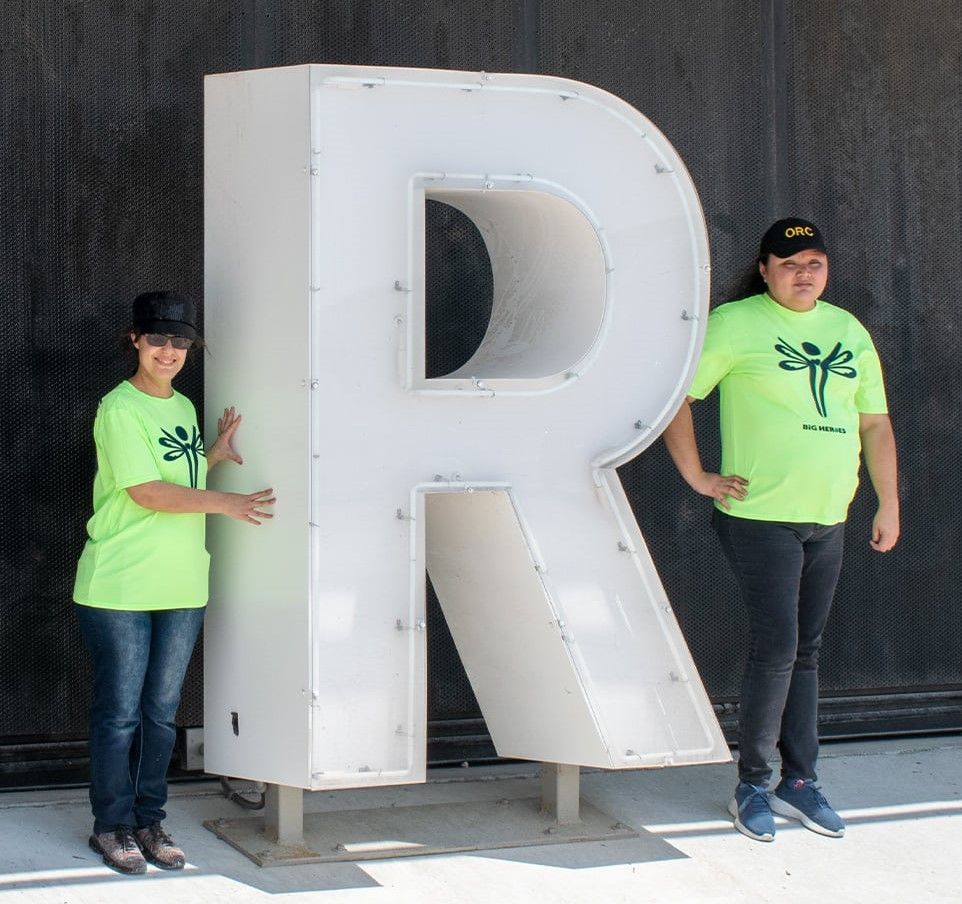 Two people standing next to a large letter r