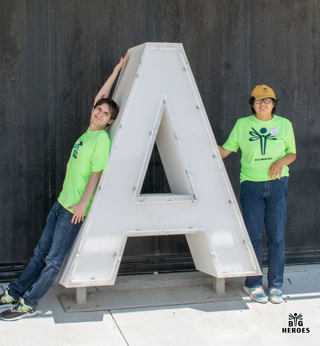 Two people standing next to a large letter a