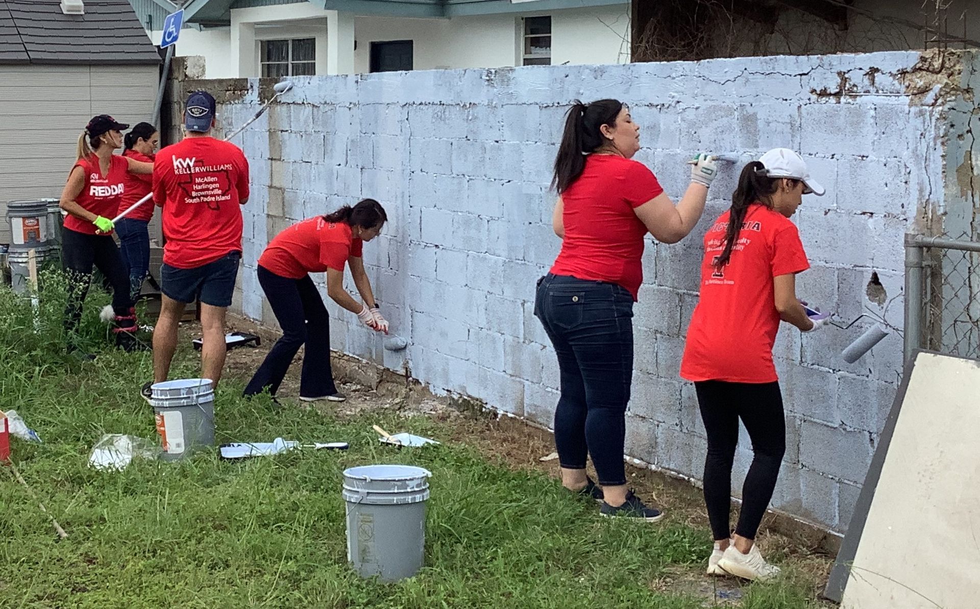 A group of women are painting a fence in a yard.