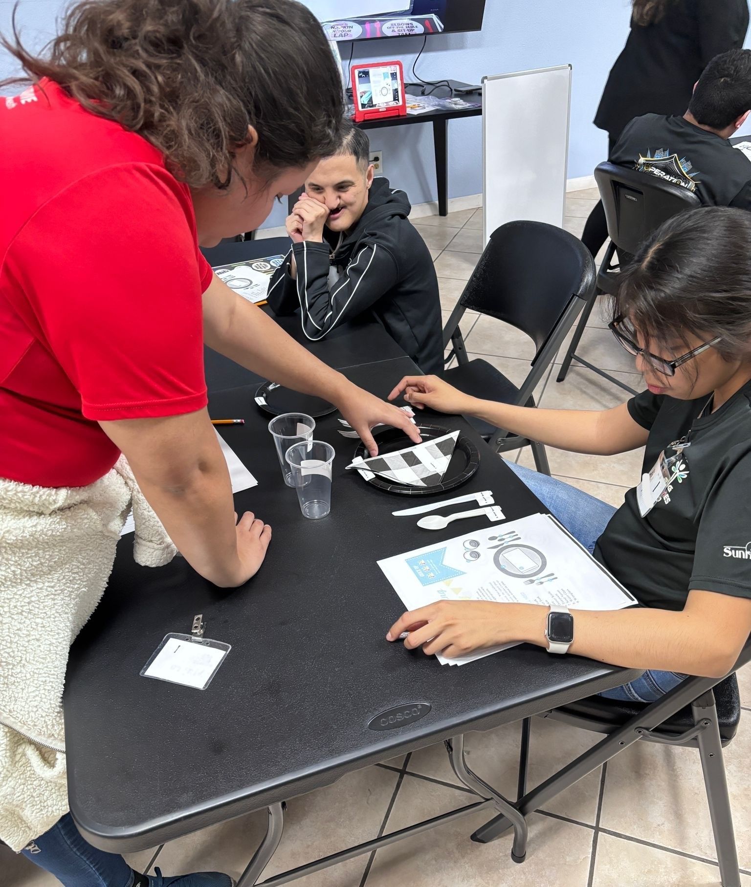 A woman in a red shirt is helping a girl with a project at a table