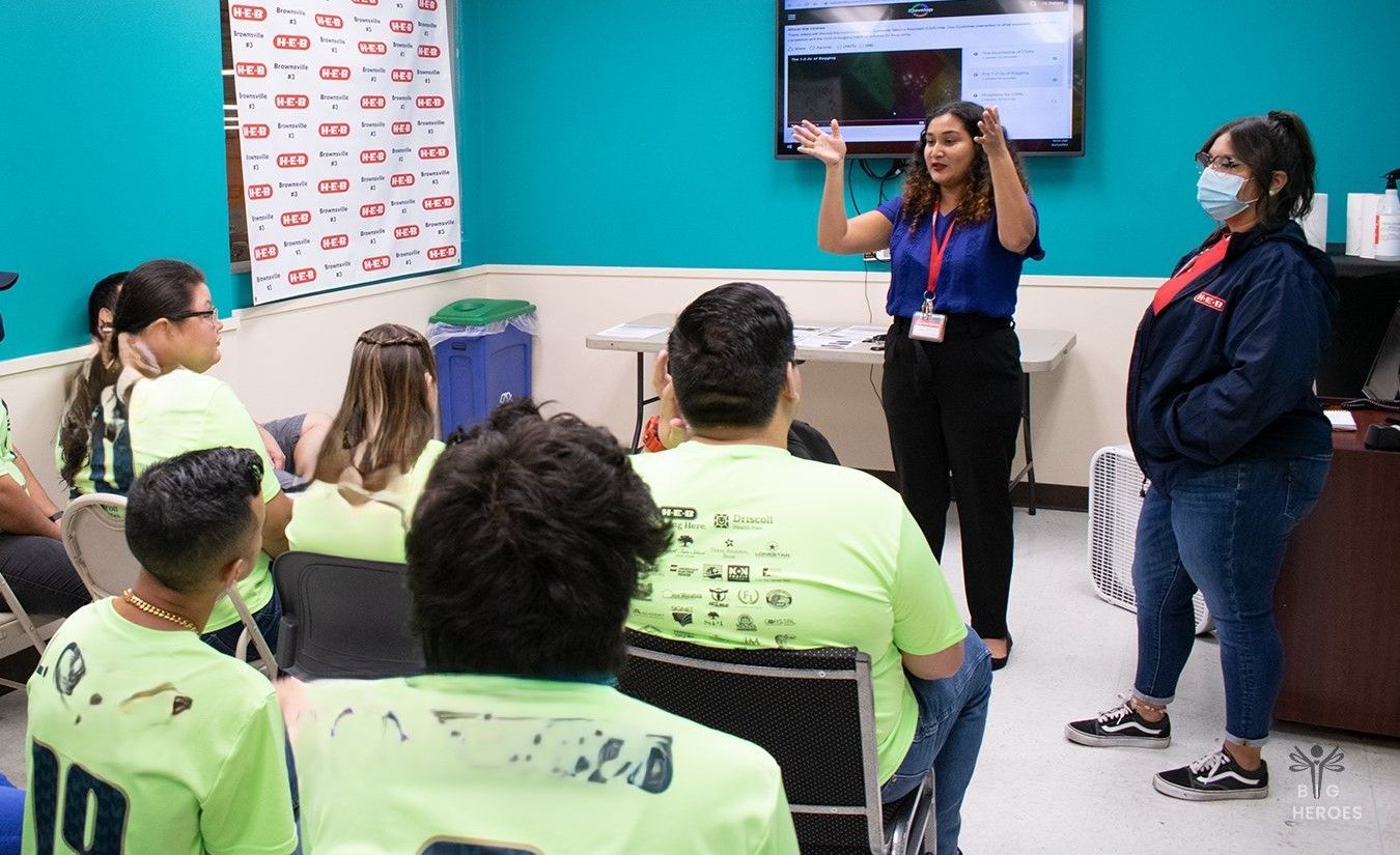 A woman is standing in front of a group of people in a room.
