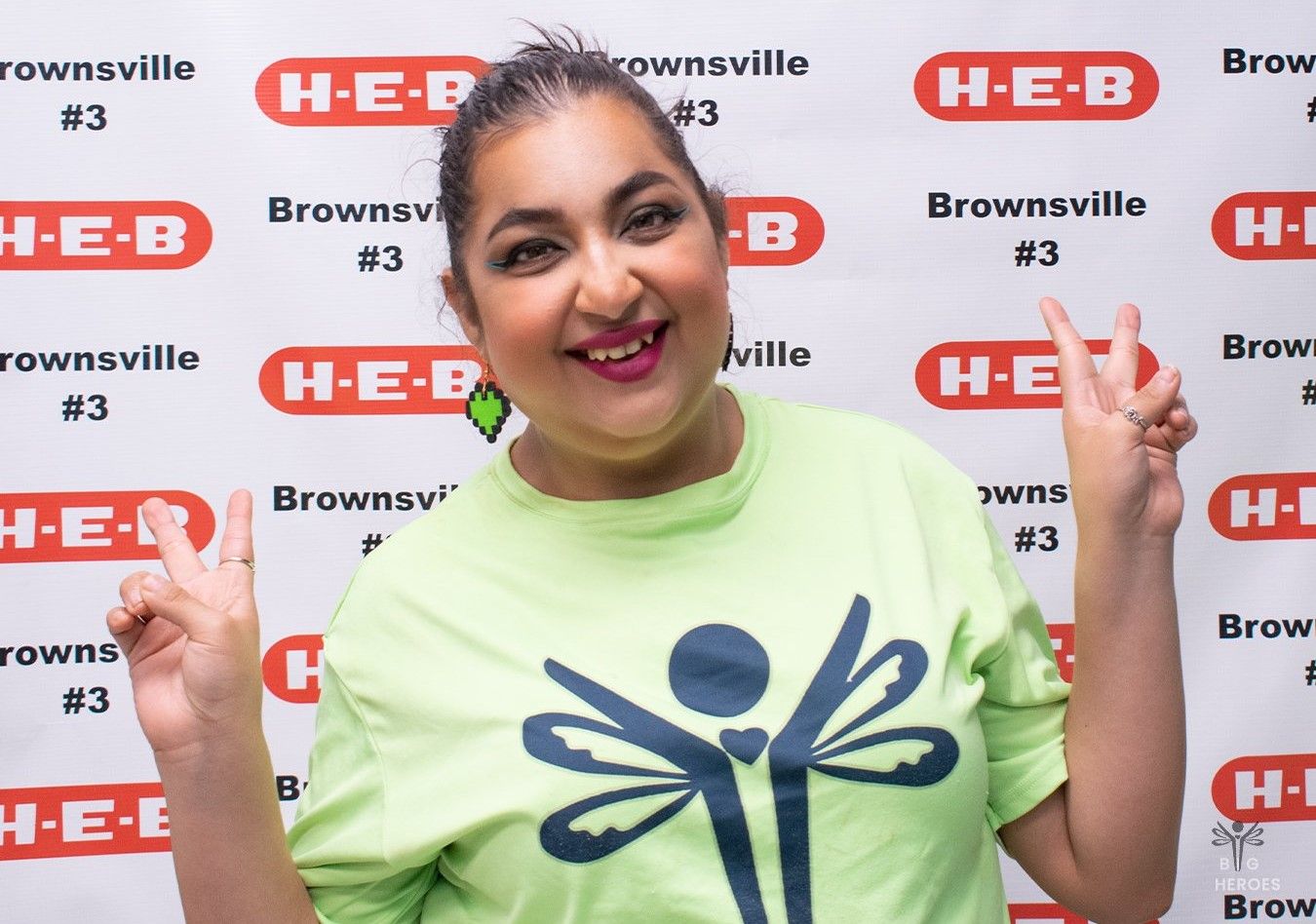 A woman in a green shirt is giving a peace sign.