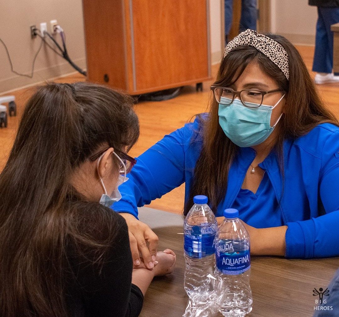 Two women wearing face masks are sitting at a table with water bottles.