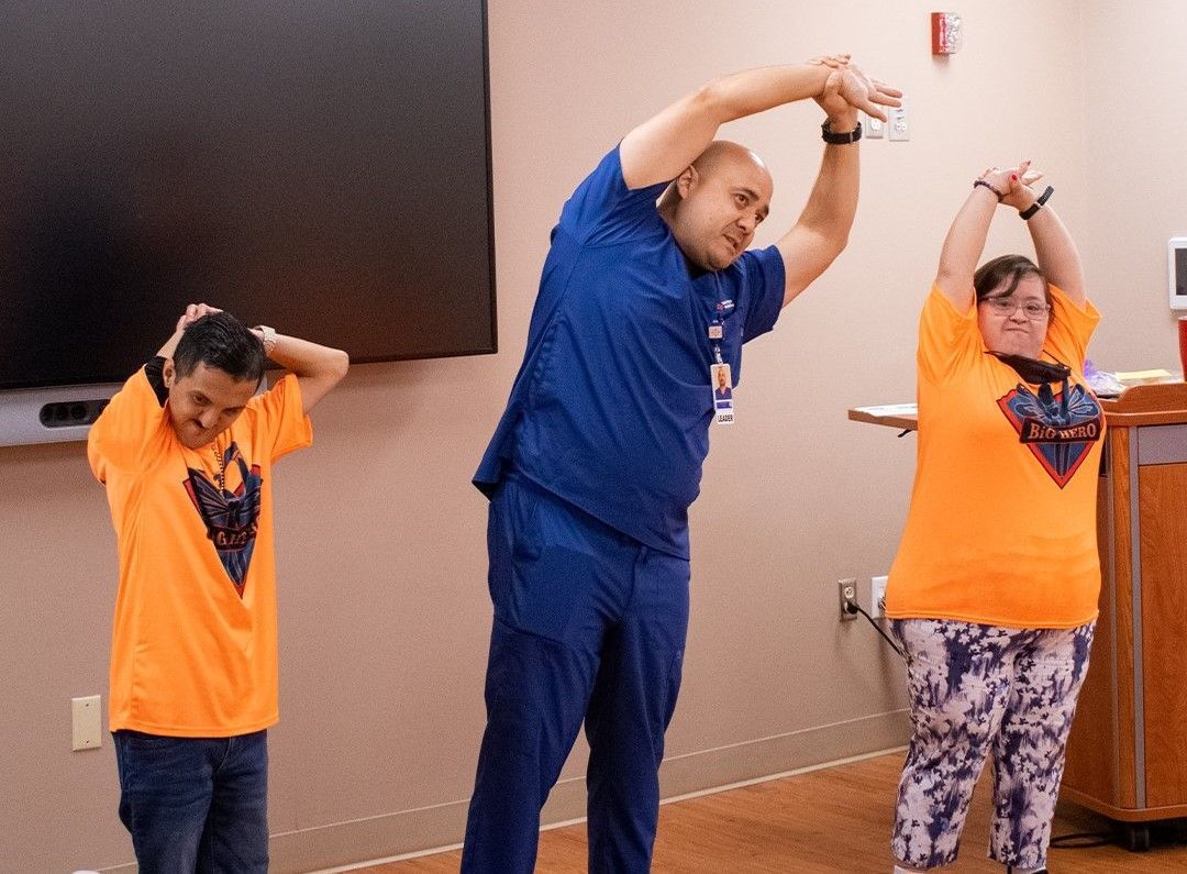 A man and two women are stretching their arms in a room.