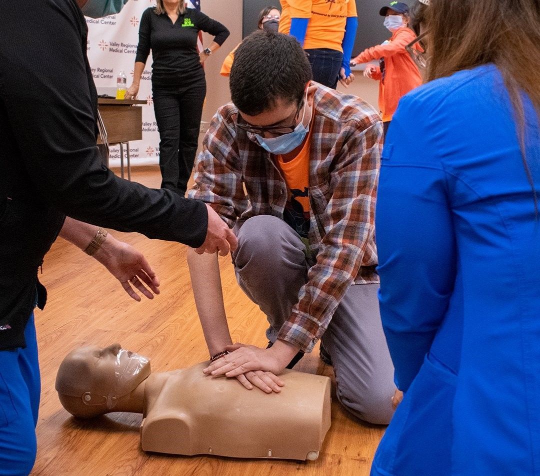 A group of people are kneeling around a mannequin on the floor.