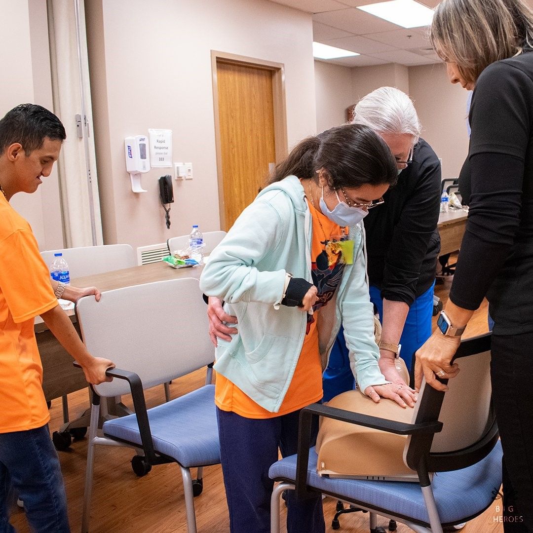A group of people are standing around a chair in a room.