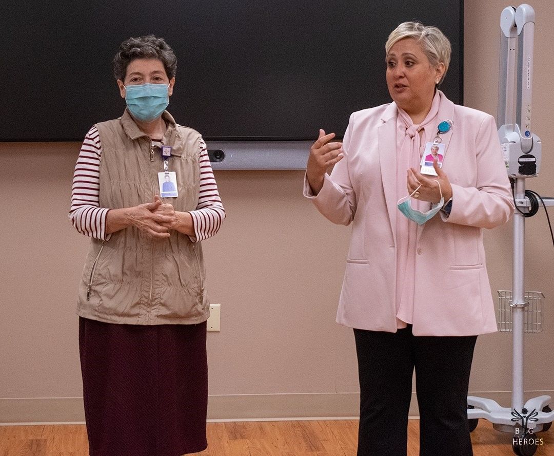 Two women wearing masks are standing next to each other in front of a blackboard.