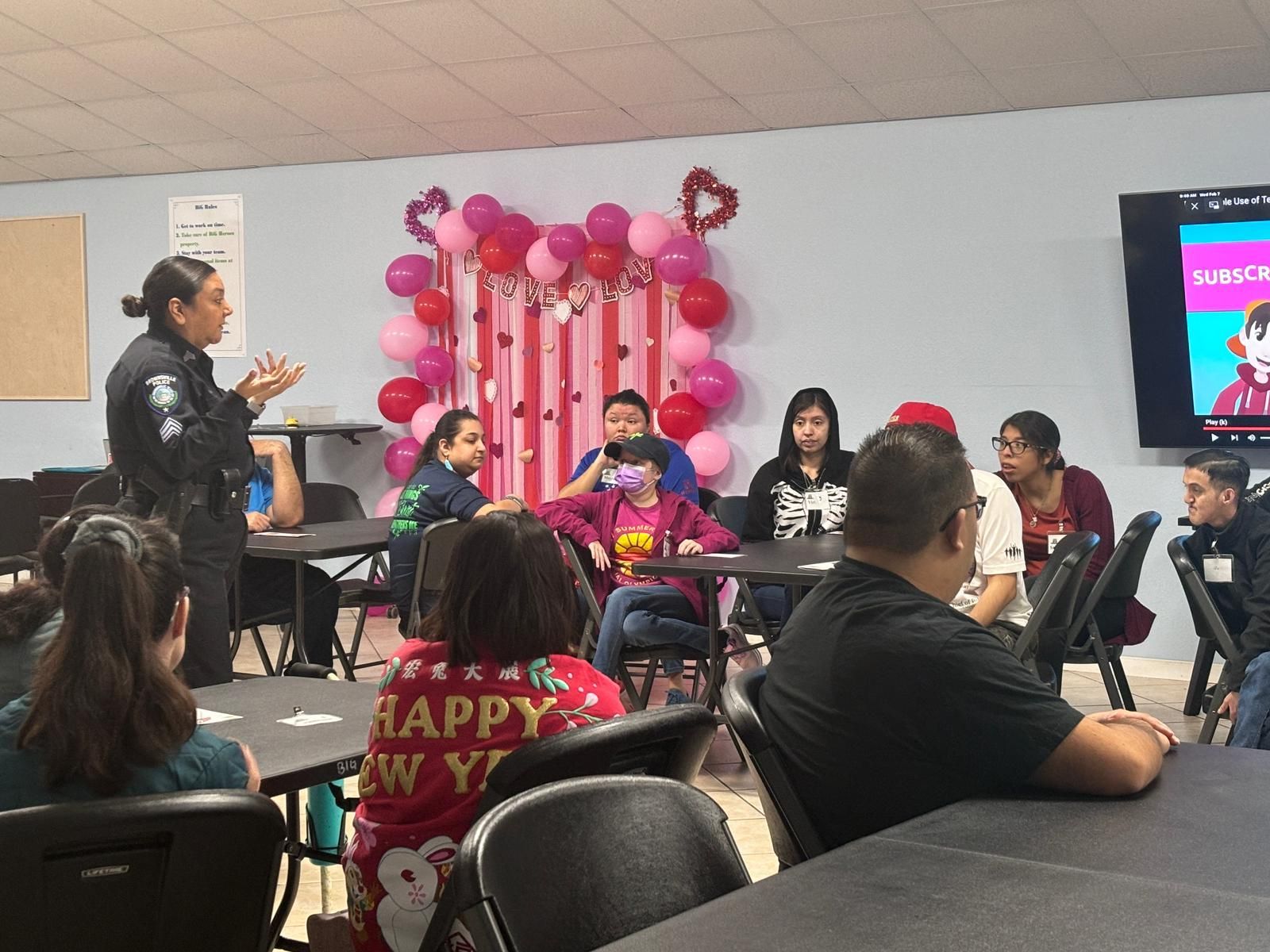 A woman is standing in front of a group of people sitting at tables.