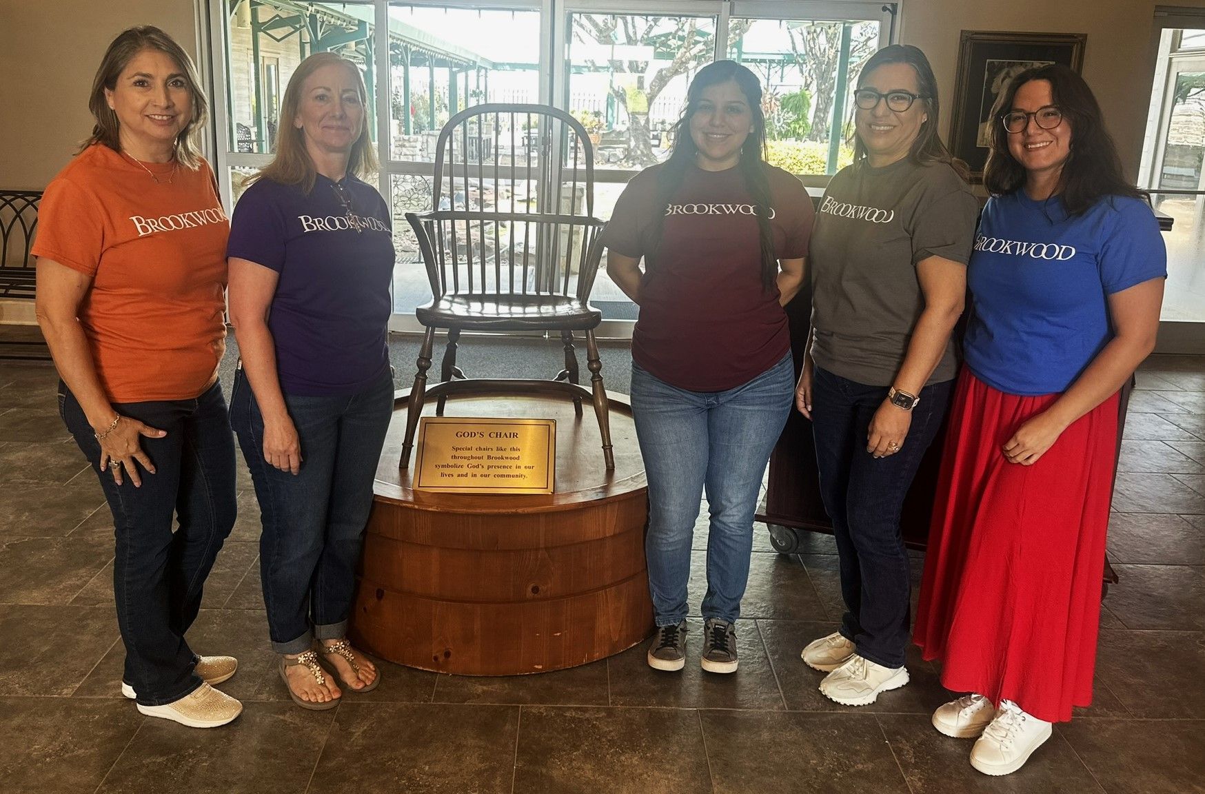 A group of women are posing for a picture in front of a wooden chair.