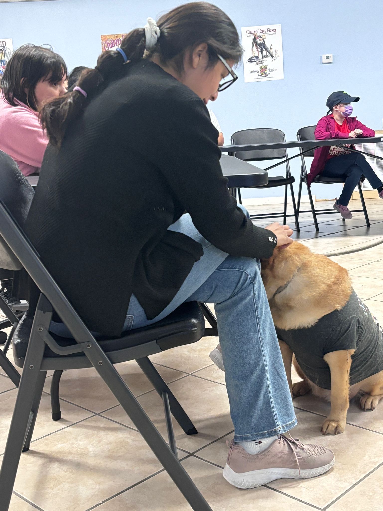 A woman is sitting in a chair petting a dog.