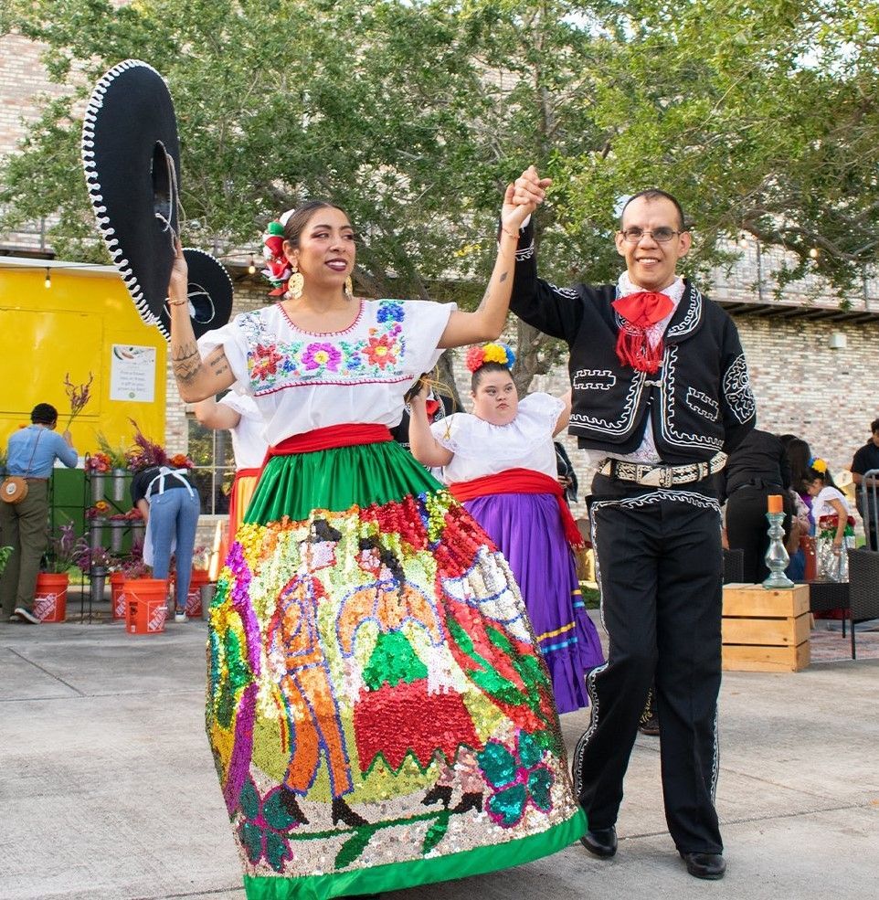 A woman in a colorful dress is dancing with a man in a mariachi outfit