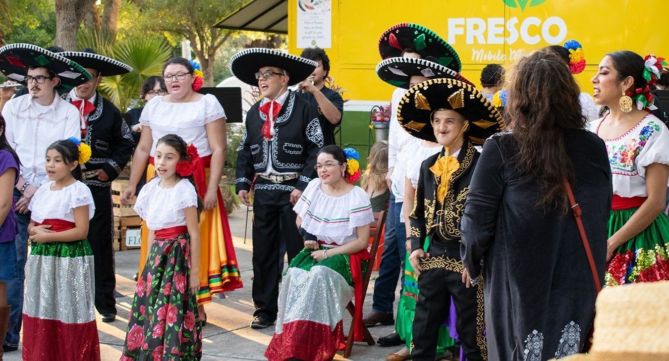 A group of people in traditional mexican costumes are dancing in front of a yellow truck.
